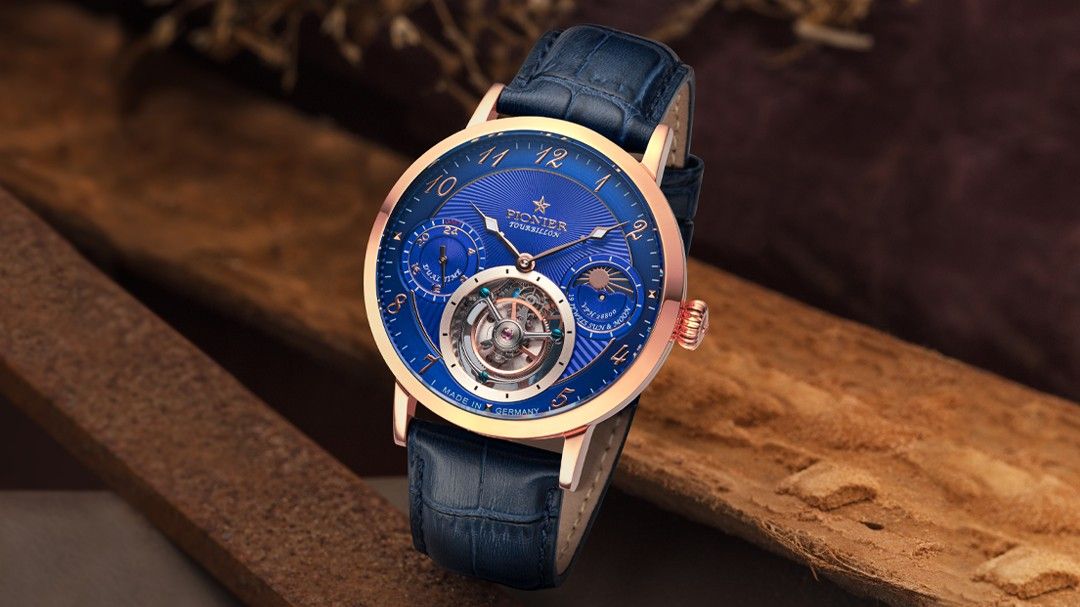 Elegant rose gold wristwatch with a deep blue dial, visible tourbillon, and blue leather strap, positioned on a rustic wooden surface.