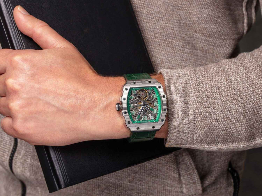 A man's wrist with a green and silver self wind watch.