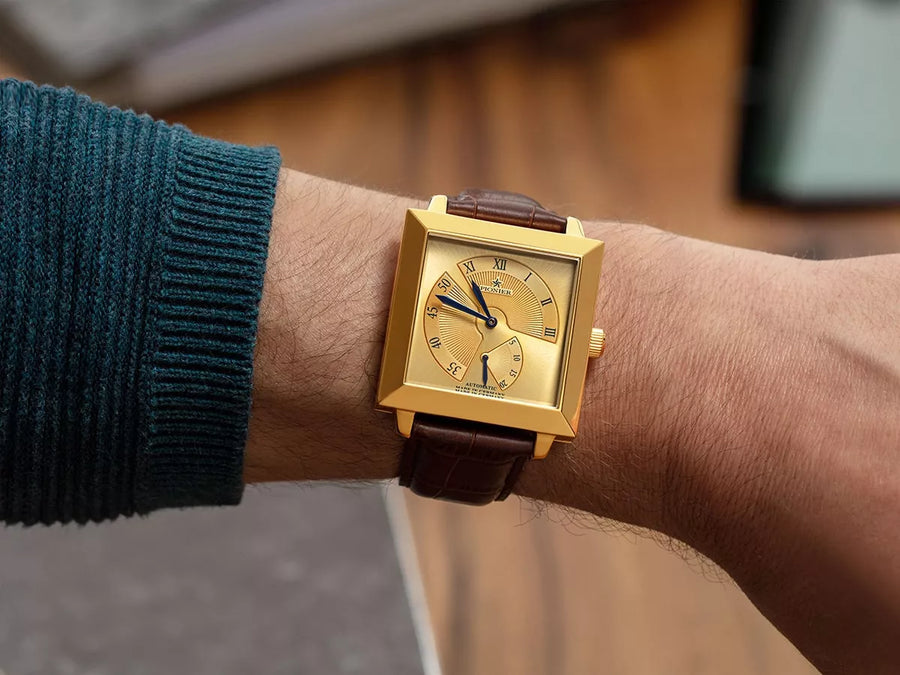 Gold color square watch with brown leather on a man's wrist.