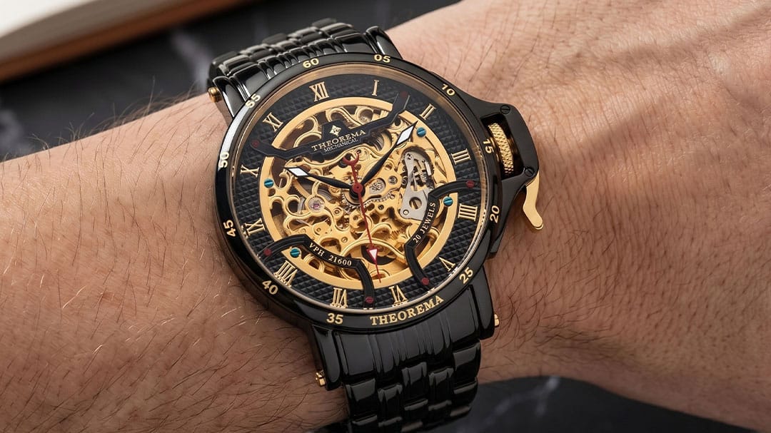 A close-up of a wrist wearing a Theoremas skeleton watch with a black metal bracelet, black case, and a gold-tone exposed mechanical dial.