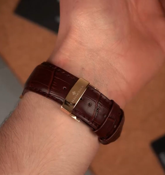 Brown leather watch strap with gold buckle on a wrist
